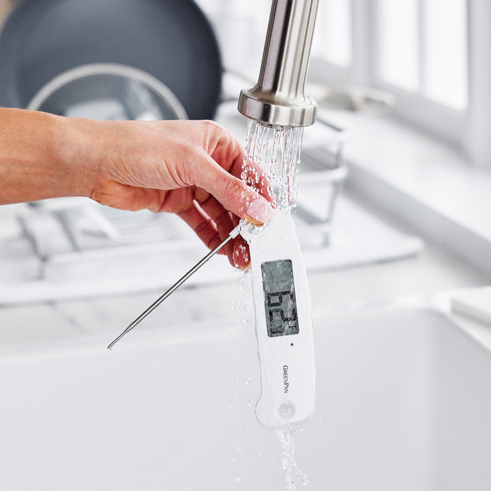 Hand rinsing a digital kitchen thermometer under running water in a sink.