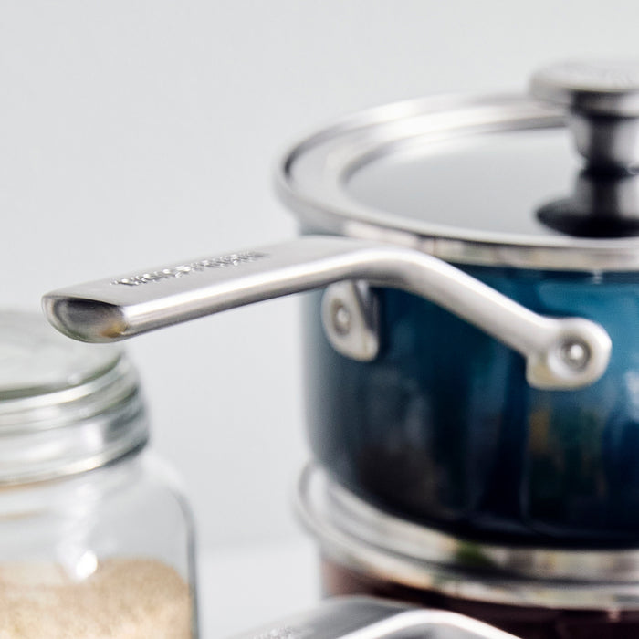 Aegean teal enameled steel saucepan with lid next to a kitchen jar on the counter.
