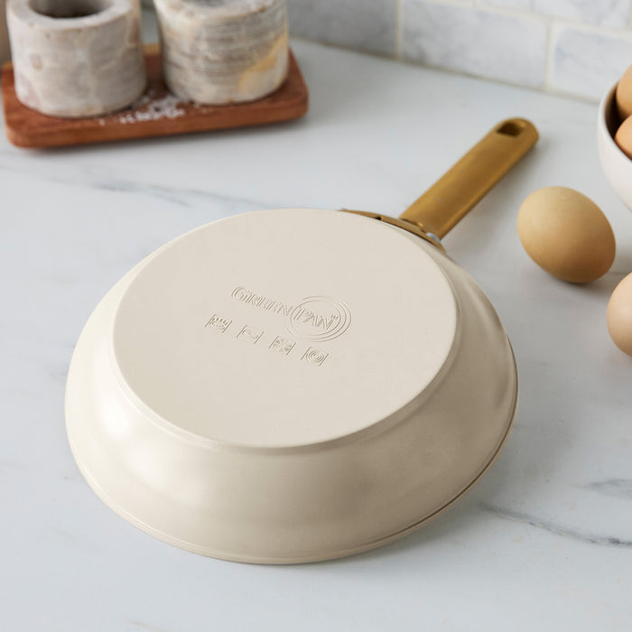 Taupe frying pan on a marble countertop with eggs and a wooden tray in the background