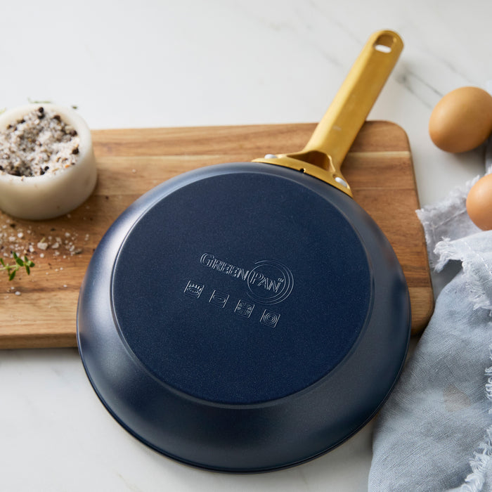 Dark blue frying pan with a gold handle on a wooden cutting board.