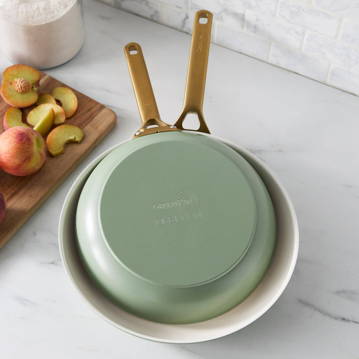 Two green frying pans with gold handles on a marble surface