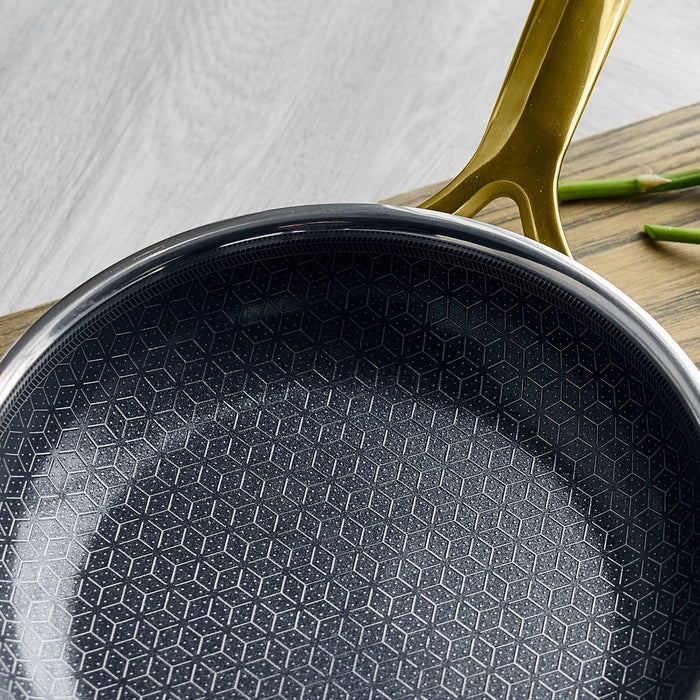 Gold ceramic nonstick frypan set on a wooden surface with asparagus beside it.