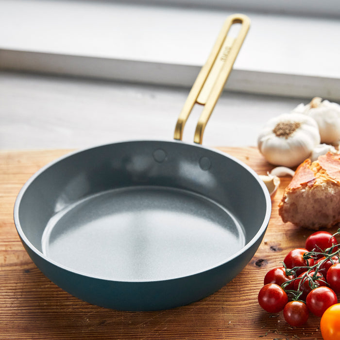 Venetian teal ceramic 8-inch frypan with gold handle on wooden counter near tomatoes and bread.
