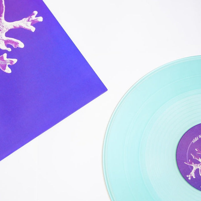 A translucent light blue vinyl from Secret Space’s The Window Room is displayed beside a purple album cover with a white abstract design on a white surface—a limited collector’s pressing from Secret Space.