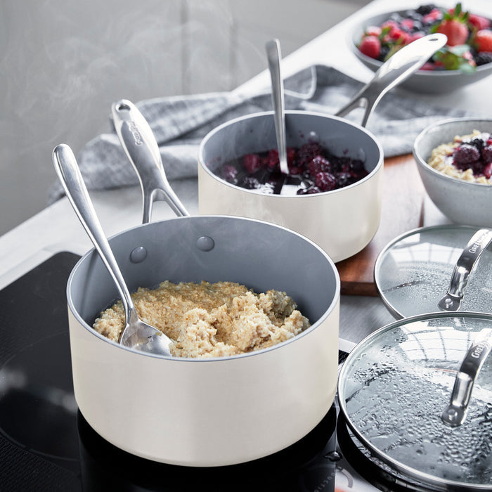 Two ceramic saucepans with lids on a stove, each simmering berry compote and holding a spoon.