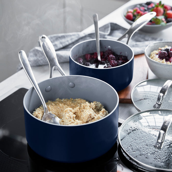 Two Valencia Pro Twilight saucepans, 1.5qt and 3qt, filled with oatmeal and berry compote, steam rising, spoons inside.