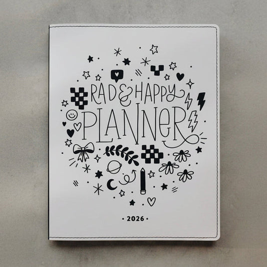 A white 2026 planner with black hand-drawn doodles and the text 'Rad & Happy Planner' on the cover, photographed flat on a textured gray surface.