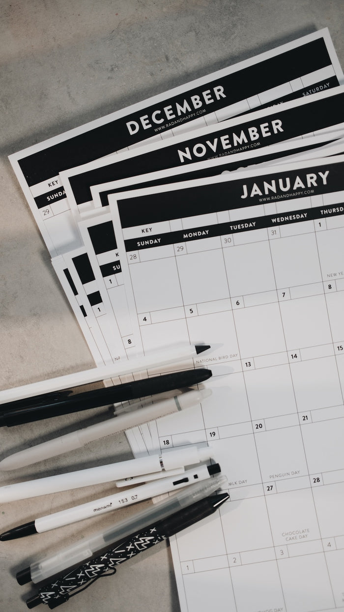Calendar sheets for December, November, and January with pens on a gray surface.