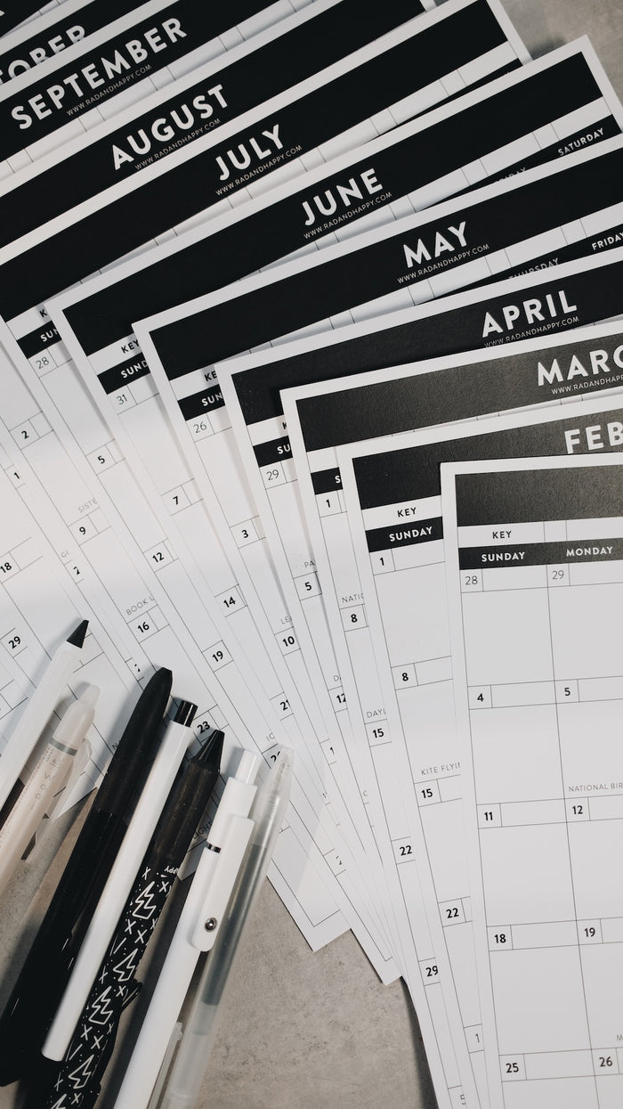 Calendar sheets with months printed on them, arranged on a flat surface with pens.