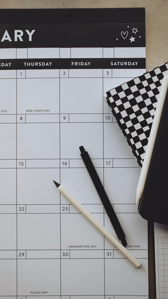 Pens and planners laying on top of a calendar on a light surface