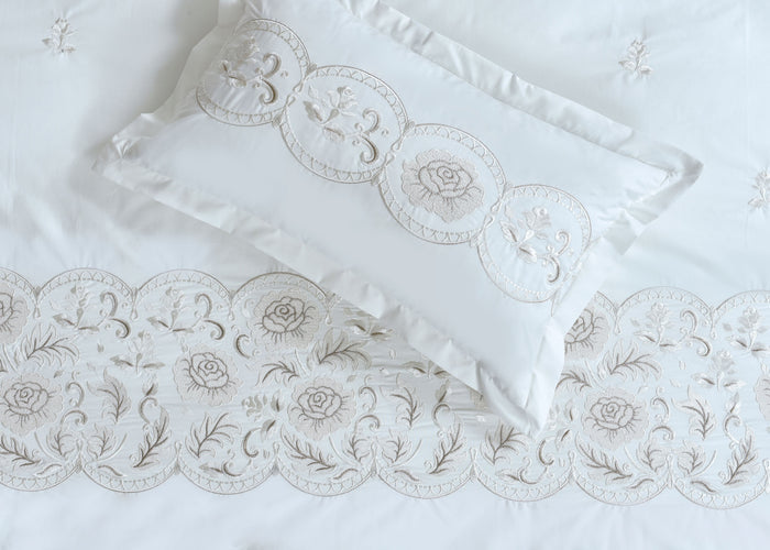 White pillow sham with embroidered circular motifs, roses, and scalloped trim