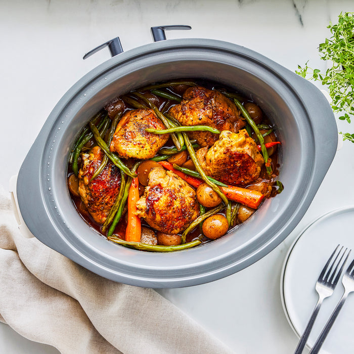 Cloud Cream slow cooker with locking lid, filled with chicken, green beans, carrots, and potatoes on a white countertop.