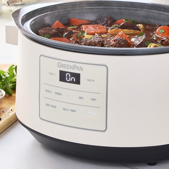Cloud Cream slow cooker with locking lid, filled with beef stew, carrots, and herbs, turned on and in use.