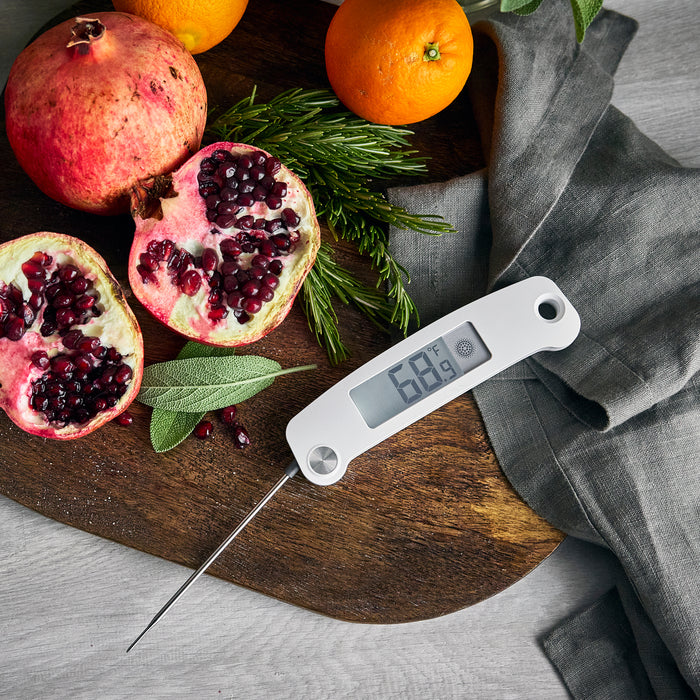 Thermometer at 68.9°F next to a bundle with pomegranate, oranges, herbs, and a knife on a cutting board.