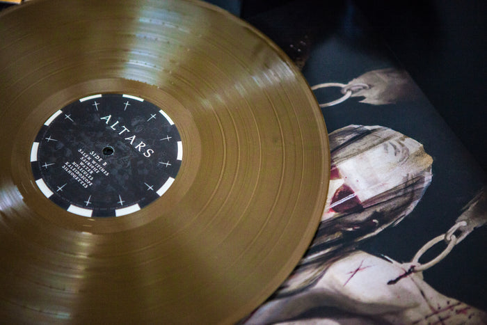 A Metallic Gold LP from Sadistik titled "Altars" rests on its cover, showing an eerie, bandaged figure with blood-stained wrappings and metal rings attached to its head and chest.