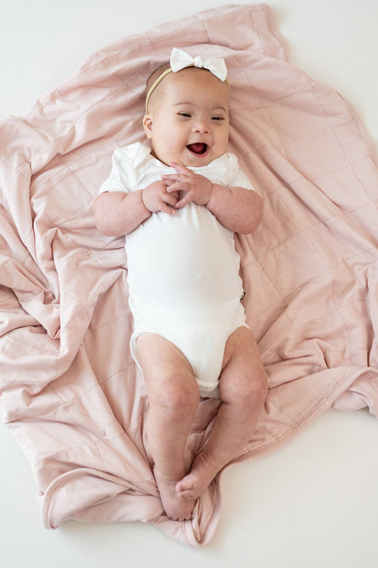 Baby wearing a Cloud Bodysuit laying on Baby Blanket in Blush 1.0