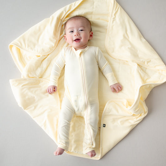 Baby in a yellow romper laying on a yellow baby blanket