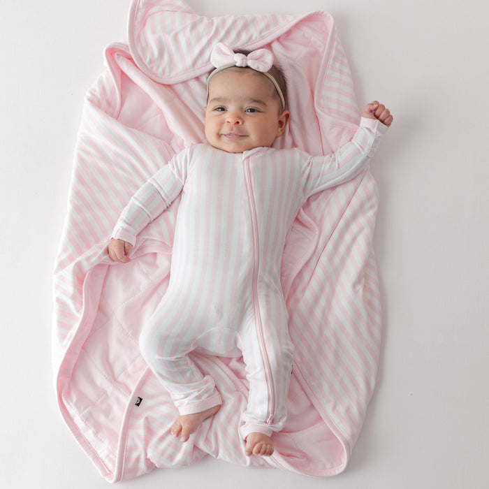 Infant girl laying on the buttery soft Baby Blanket in Small Sakura Stripe 1.0 wearing a matching zippered romper