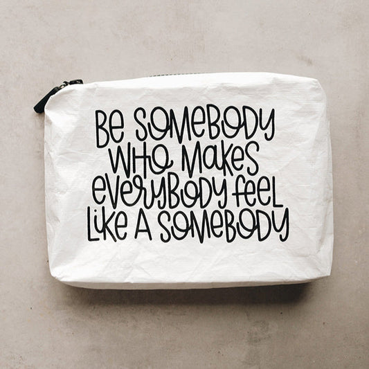 A white Tyvek zipper pouch with the text 'BE SOMEBODY WHO MAKES EVERYBODY FEEL LIKE A SOMEBODY' written in black.