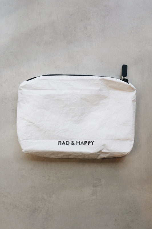 White tyvek zipper pouch with the text Rad & Happy written in black sitting on a gray surface