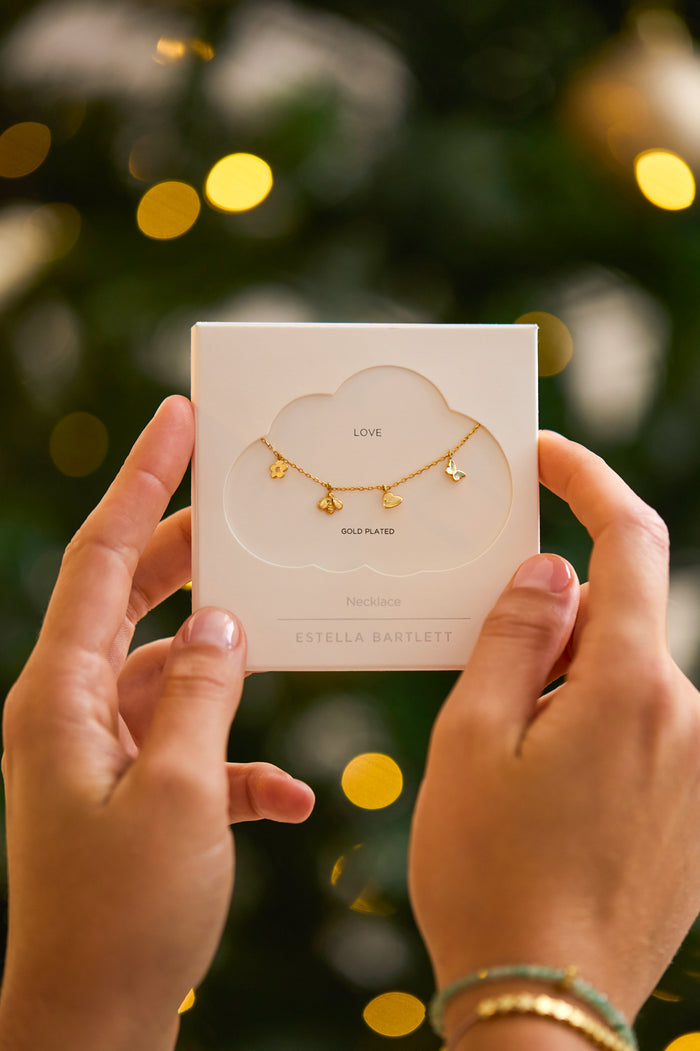 Hands holding a jewelry box with a necklace design against a blurred festive background