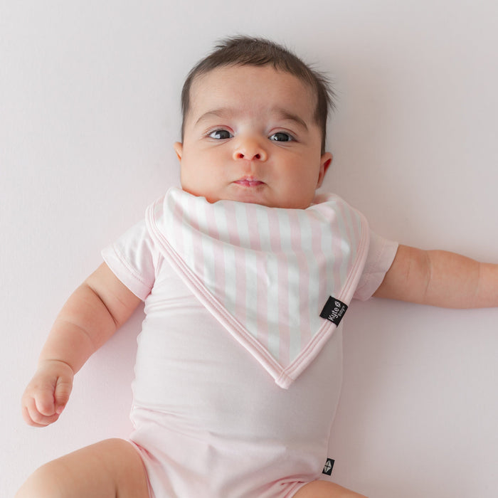 Close up of infant wearing the Bib in Small Sakura Stripe wearing a Sakura pink short sleeve bodysuit laying on a  pink blanket