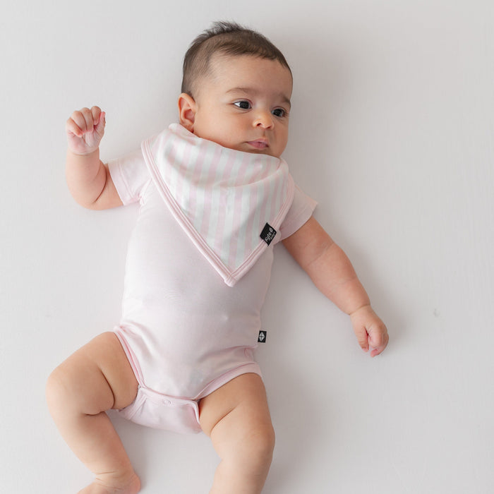 Young infant laying on a pink blanket wearing the absorbent Bib in Small Sakura Stripe paired with a short sleeve bodysuit in Sakura