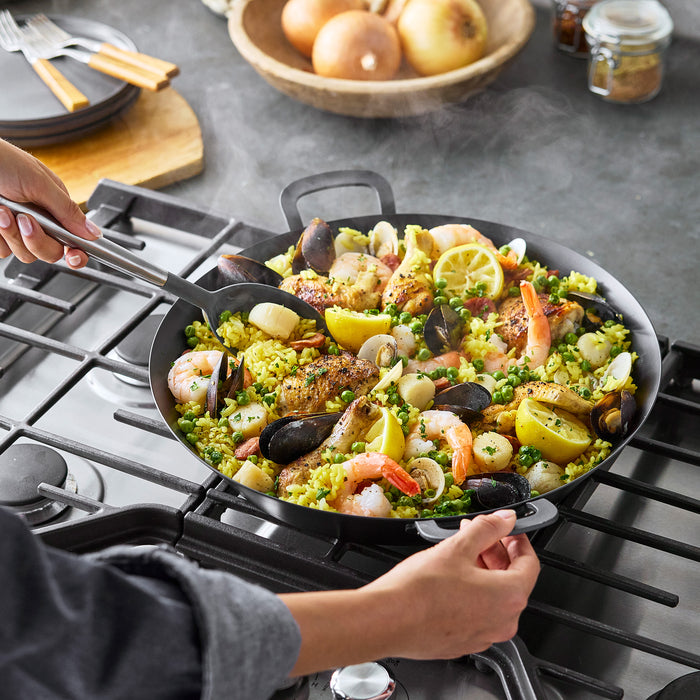 Seafood paella being served from a carbon steel pan with fresh ingredients arranged around it.
