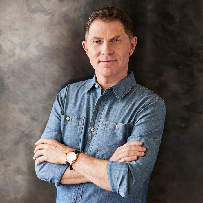 Man in a blue shirt stands with arms crossed next to a stainless steel 10-piece cookware set.