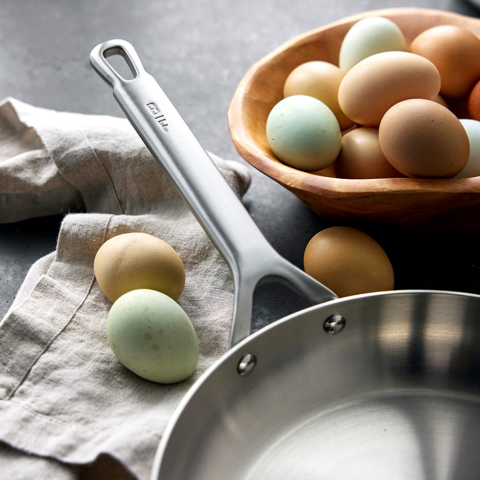 GreenPan Chef Series frypan set with two silver pans, a white cloth, and brown eggs in a wooden bowl on a dark counter.