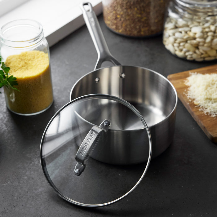 Stainless steel saucepan with glass lid on a dark countertop.