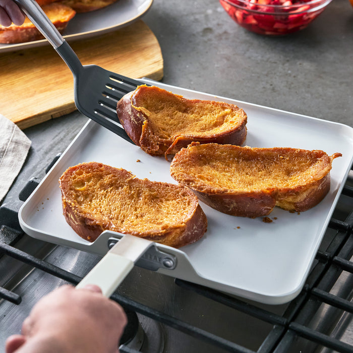 Three slices of French toast on a GreenPan 11-inch ceramic nonstick square griddle on a stovetop.