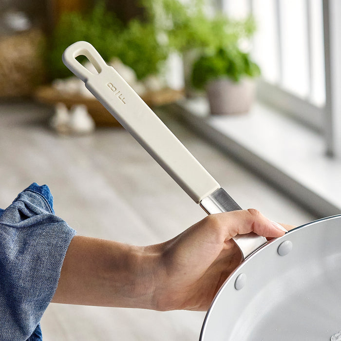 Chef holding a spatula above a cream GreenPan Bobby Flay 12-inch frypan in a bright kitchen.