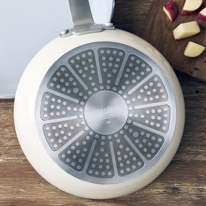 Cream ceramic nonstick frypan with handle next to chopped red potatoes on a light surface.