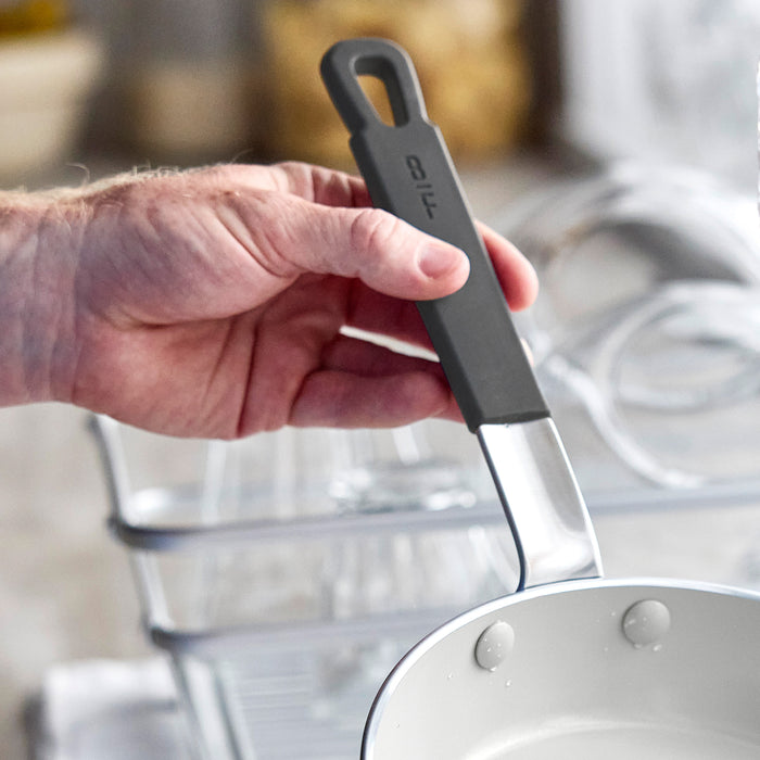 Person holding a 12-inch ceramic nonstick frypan with metal handle above a dish rack with glassware.