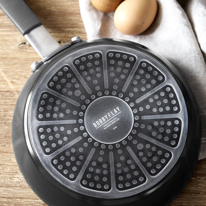 Gray 12-inch Bobby Flay by GreenPan frypan on wood surface with two brown eggs and a beige cloth nearby.