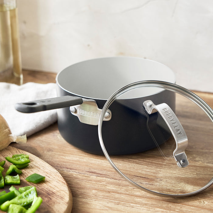 Ceramic nonstick saucepan with lid on a counter beside chopped green peppers.