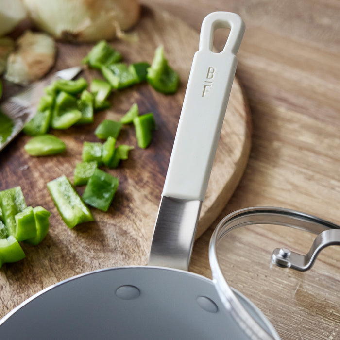 Cream ceramic nonstick saucepan with lid next to chopped green pepper and onion.