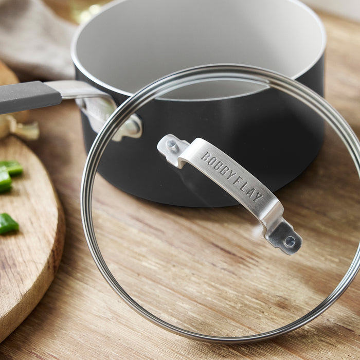 Small saucepan with lid next to a wooden board topped with chopped green onions.