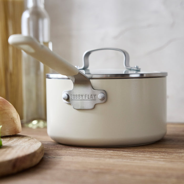 Cream ceramic nonstick saucepan with lid on a wooden countertop. 1.6-quart size, single piece shown.