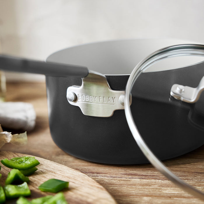 GreenPan 1.6-quart saucepan with lid on wood surface next to sliced green peppers.