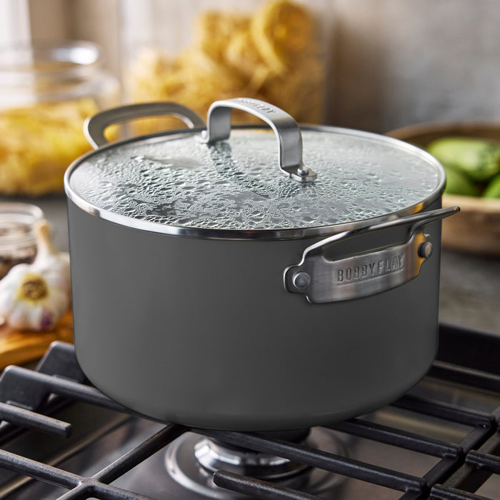 Gray 6-quart GreenPan stockpot with lid on a stove, blurred kitchen items in the background.