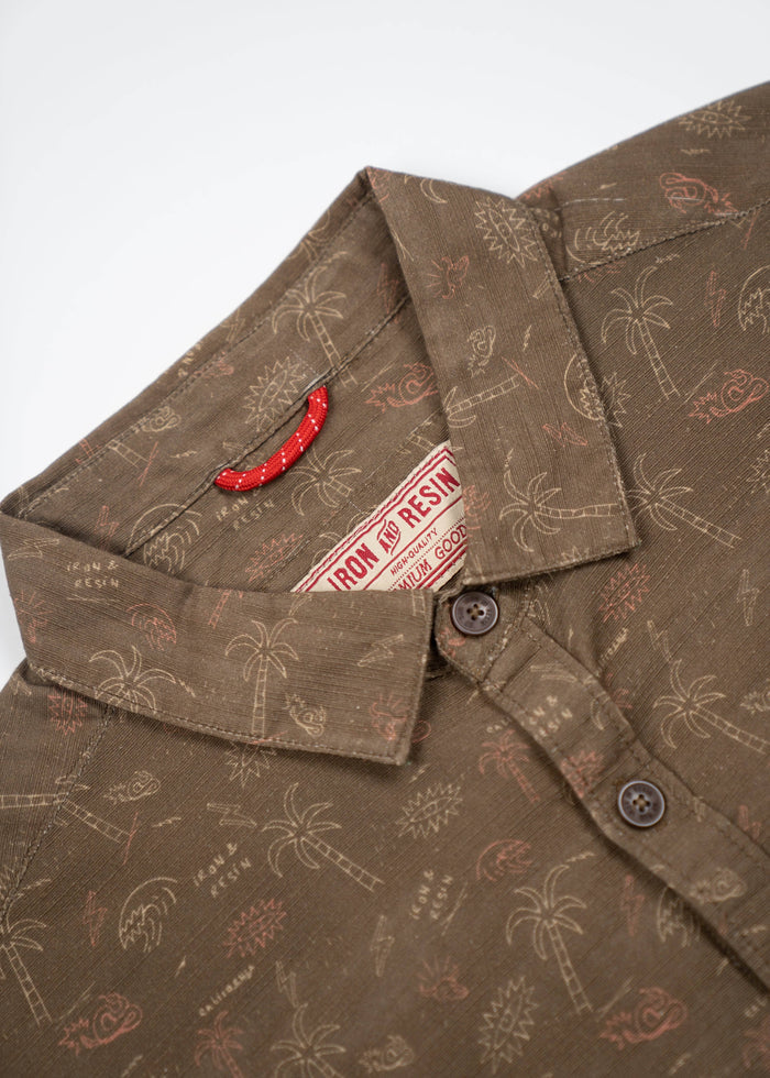 Brown shirt with palm tree and sun patterns, featuring a red tag labeled "Iron & Resin" near the collar and button details.