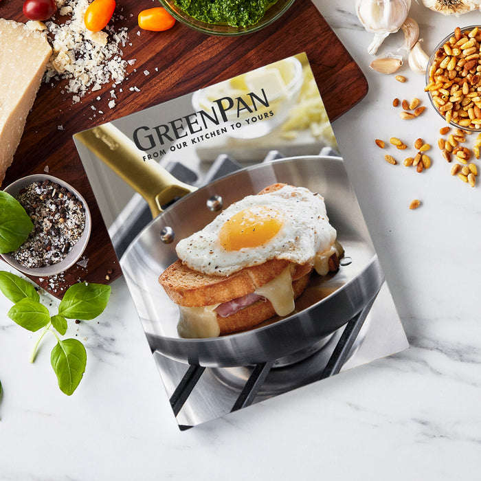 The Cook's Journal Cookbook, Vol. 2 sits on a marble countertop, its cover showing a fried egg sandwich with basil, salt, parmesan cheese, pine nuts, tomatoes, pesto, and garlic—perfect inspiration for discovering new recipes.