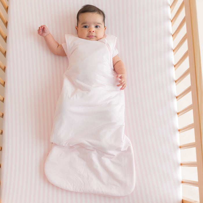 Infant laying in a crib on the Crib Sheet in Small Sakura Stripe wearing a Sakura pink sleep bag