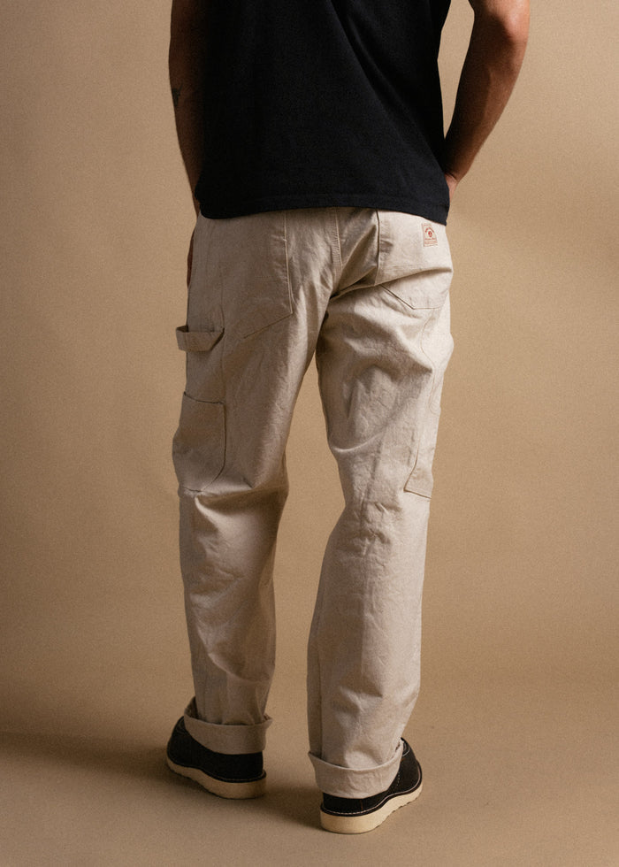 Man in black shirt and beige cargo pants stands against a neutral background, hands in pockets, showcasing casual style.