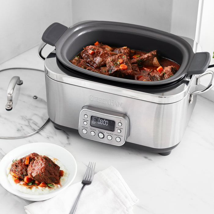 Stainless steel slow cooker with digital display on a marble countertop, containing stewed meat and vegetables.