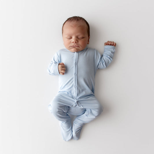 Newborn baby in a light blue footie lying on a white surface