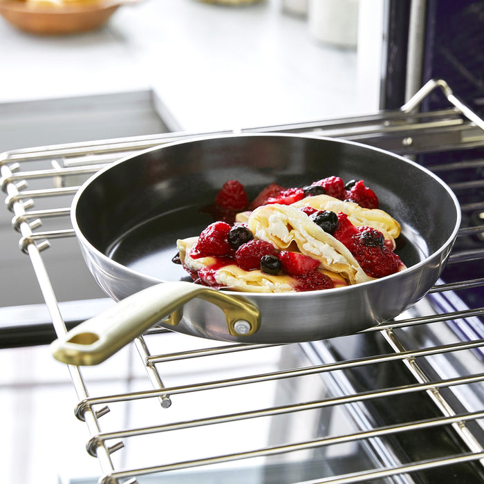 Pancakes with berries in a stainless steel 12-inch frypan with lid and champagne handles on a kitchen surface.
