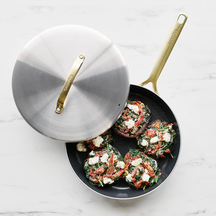 Stuffed mushrooms with spinach, tomato, and cheese in a stainless steel frypan with champagne gold handles.